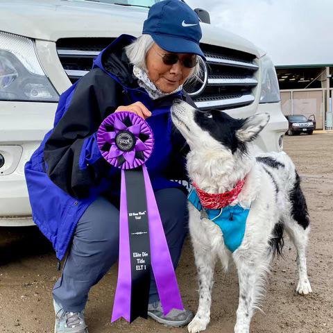 A person hugging a dog and holding a purple award ribbon