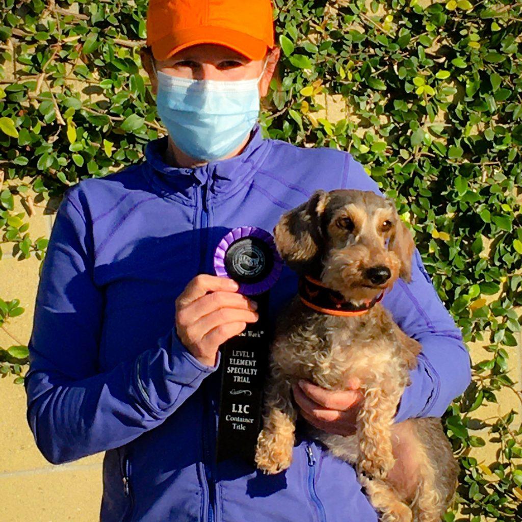 A person holding a recognition ribbon in one hand and carrying a dog in the other